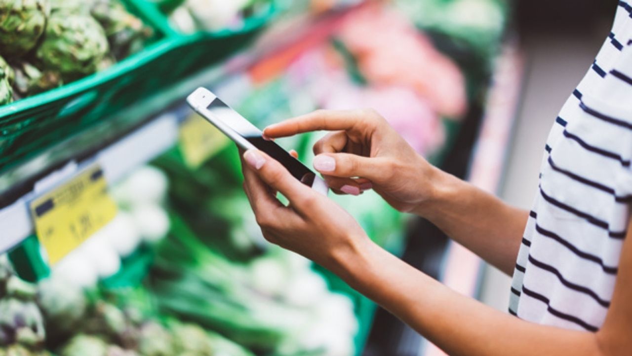 Frau steht mit ihrem Handy in der Obst- und Gemüseabteilung