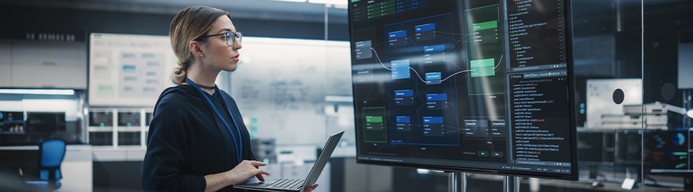 Consultant working on a laptop while looking at a giant screen