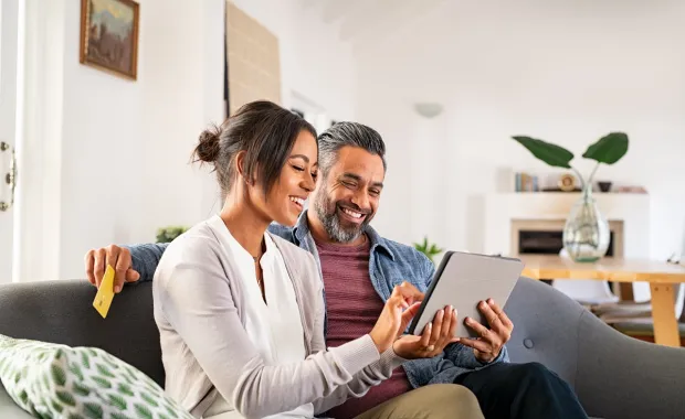 Couple sitting on a couch smiling while looking at a tablet