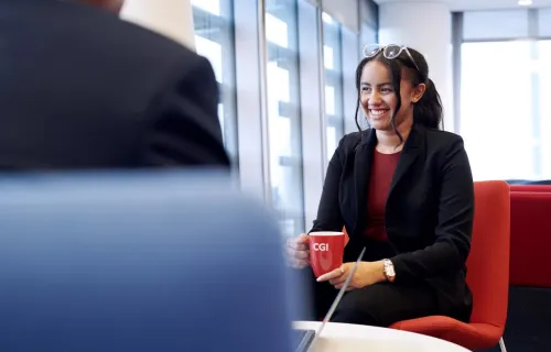 Kuvassa CGI:n konsultti pitelee kahvikuppia ja hymyilee