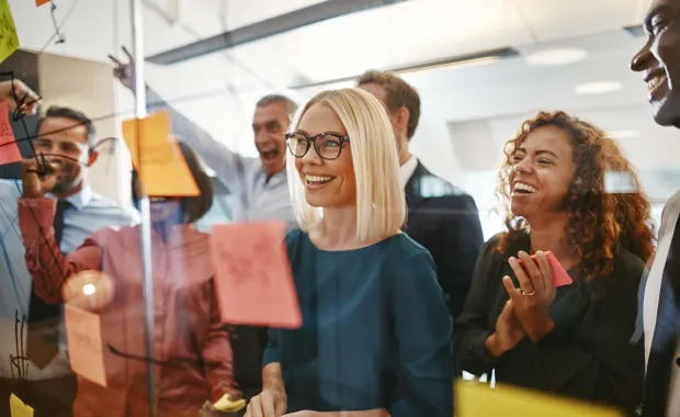 A team of people smiling while working collaboratively around an Agile project board