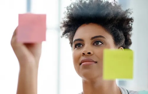 Frau klebt beschriftet bunte Post-it auf einer Glaswand