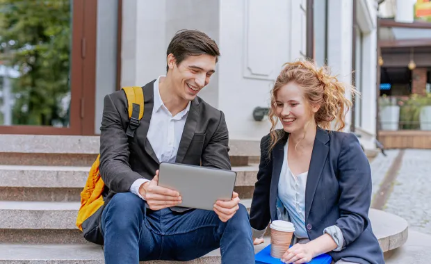 A male and female sitting outside on steps looking at a tablet and smiling